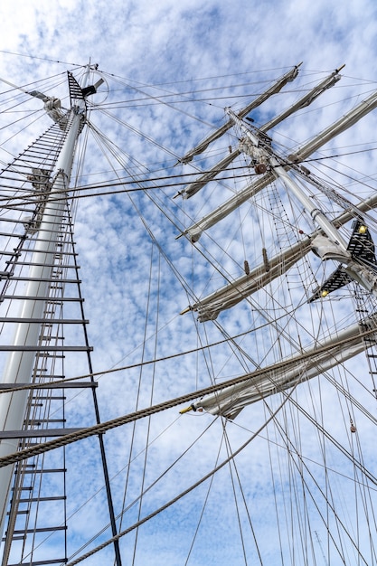 Inquadratura dal basso degli alberi, del sartiame e delle funi di una grande nave a vela sotto un cielo nuvoloso