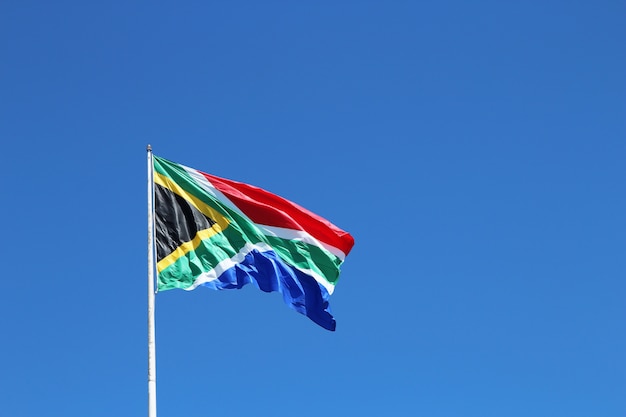 Inquadratura dal basso della bandiera sudafricana nel vento sotto il cielo blu chiaro