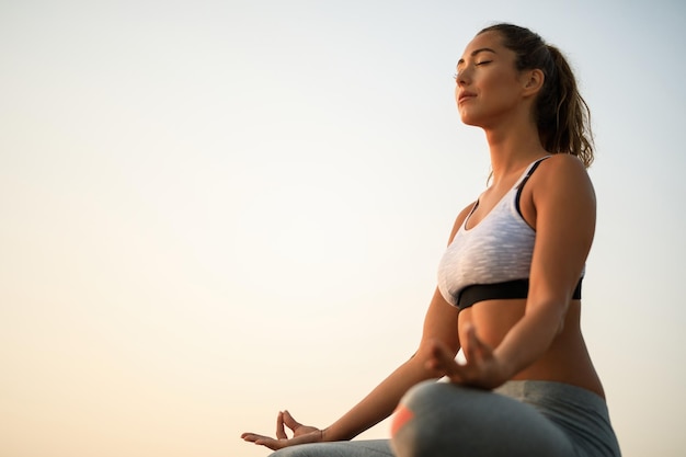 Inquadratura dal basso della donna con gli occhi chiusi che praticano Yoga contro il cielo. Copia spazio.