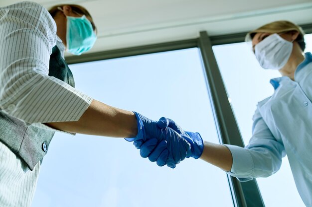Inquadratura dal basso di colleghi di lavoro che indossano guanti protettivi mentre si stringono la mano in ufficio durante l'epidemia di coronavirus