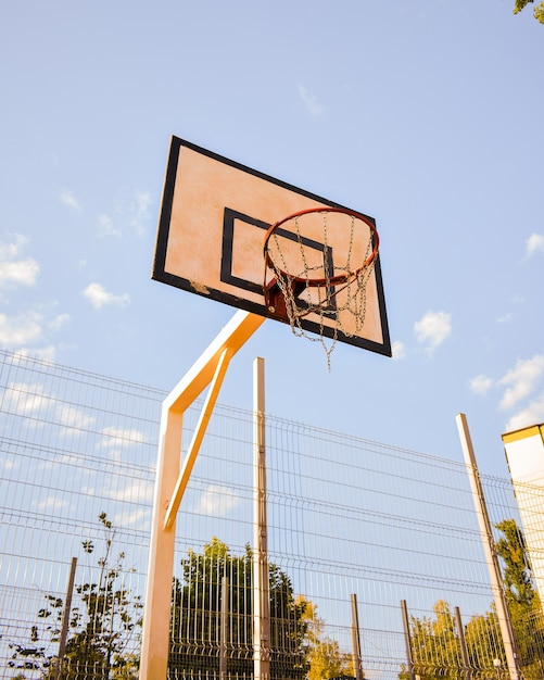 Inquadratura dal basso di un anello di pallacanestro con rete a catena contro un cielo nuvoloso blu