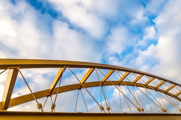 Inquadratura dal basso di un ponte strallato giallo con un cielo nuvoloso blu