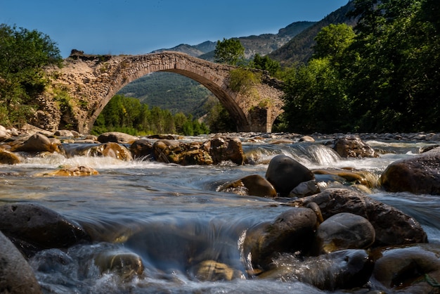 Inquadratura dal basso di un vecchio ponte ad arco con un fiume sotto di esso durante la luce del giorno