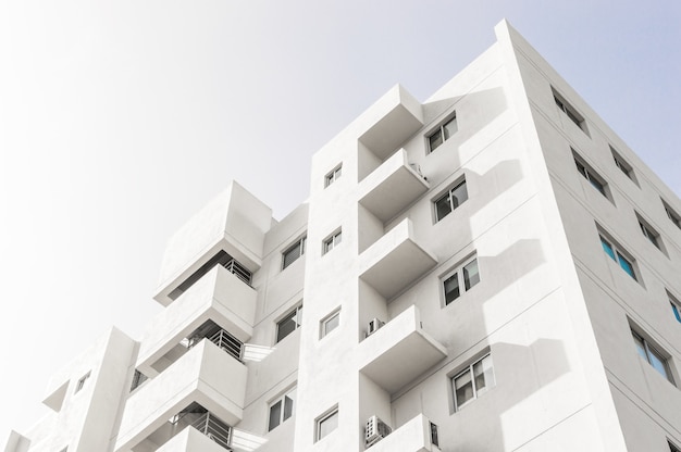 Inquadratura dal basso di una facciata di un edificio moderno bianco sotto un cielo azzurro chiaro