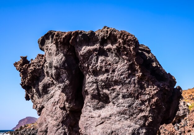 Inquadratura dal basso di una grande roccia su una spiaggia con un cielo blu chiaro