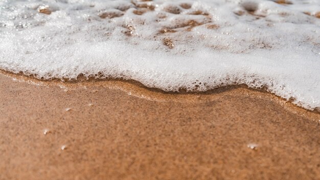 Inquadratura dall'alto delle onde spumose che arrivano verso la spiaggia sabbiosa