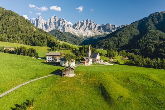 Inquadratura dall'alto di molti edifici circondati da alte montagne rocciose in Val di Funes