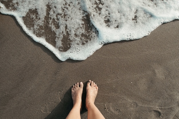 Inquadratura dall'alto di una persona in piedi sulla spiaggia vicino alla schiuma di mare