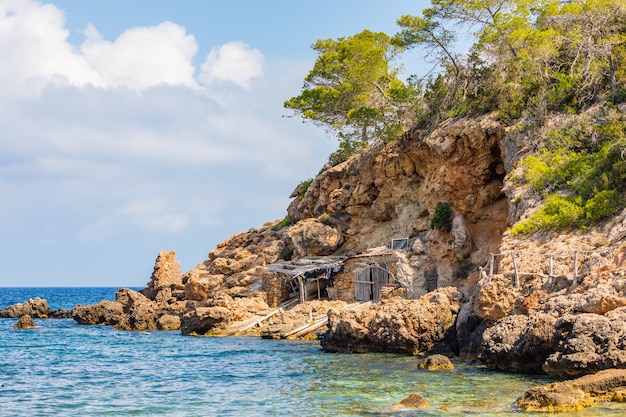 Inquadratura di una baracca in riva al mare, costruita sotto la scogliera circondata da grossi pezzi di pietra