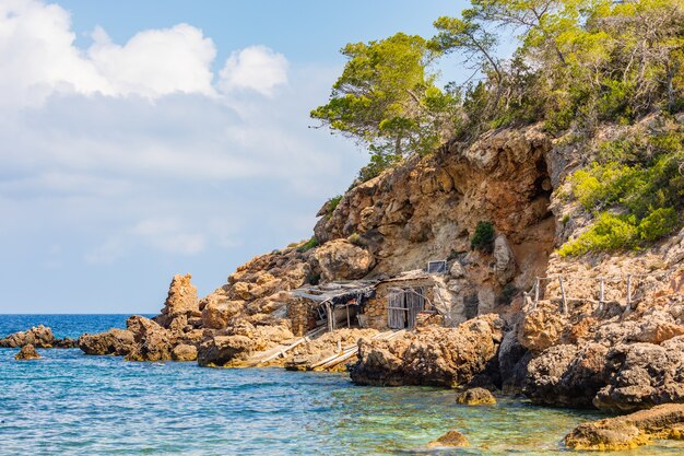 Inquadratura di una baracca in riva al mare, costruita sotto la scogliera circondata da grossi pezzi di pietra