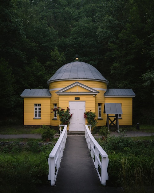 Inquadratura frontale verticale di una struttura cristiana gialla con una strada sottile e un giardino davanti a una foresta
