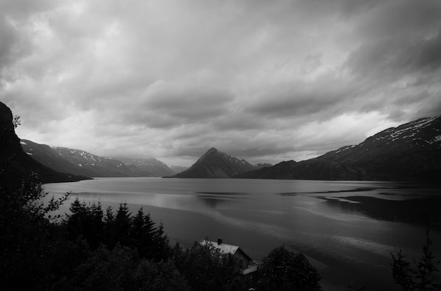 Inquadratura in scala di grigi del lago circondato da montagne e alberi