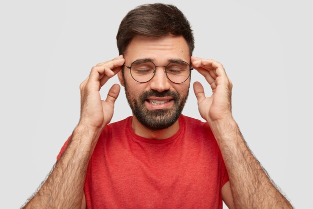 Inquadratura orizzontale di bell'uomo con la barba lunga con i capelli scuri, tiene le mani sulle tempie, chiude gli occhi