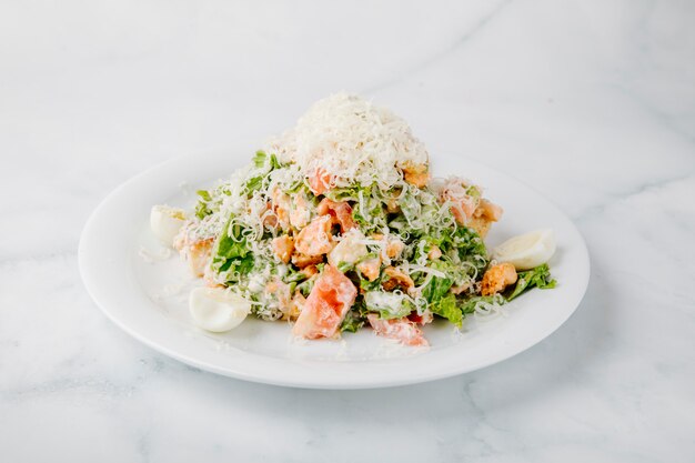 Insalata Caesar con ingredienti misti e formaggio tritato sulla parte superiore in sfondo bianco.