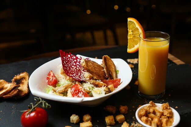 Insalata caesar di pollo vista frontale su un piatto con succo d'arancia e crostini di pane sul tavolo