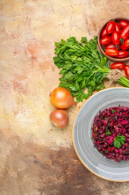 Insalata di barbabietola sana vista dall'alto su un piatto grigio con verdure fresche per la sua preparazione su uno sfondo di legno con spazio libero per il testo