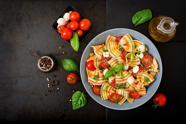 Insalata di farfalle di pasta colorata con pomodori, mozzarella e basilico.