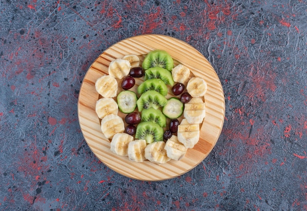 Insalata di frutta con banana a fette, kiwi e frutti di bosco in un piatto di legno.
