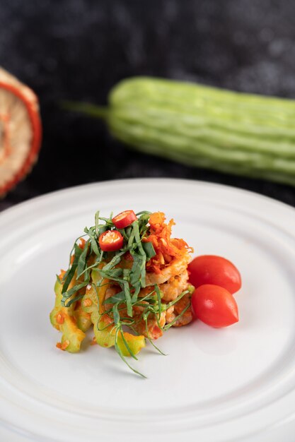 Insalata di maiale lime piccante con melone amaro, galanga, peperoncino, pomodori e aglio in un piatto bianco su un pavimento di cemento nero.