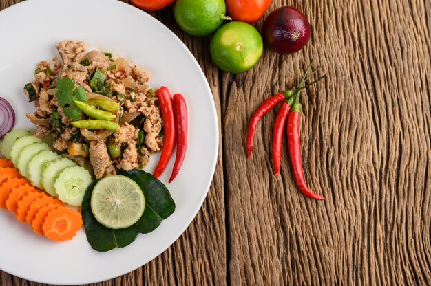 Insalata di maiale tritata piccante su un piatto bianco sulla tavola di legno.