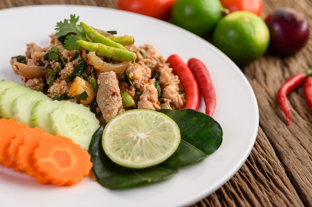 Insalata di maiale tritata piccante su un piatto bianco sulla tavola di legno.