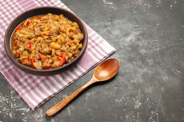 Insalata di melanzane arrostite vista dal basso in ciotola su tovaglia a scacchi bianca rosa cucchiaio di legno su spazio copia tavolo scuro