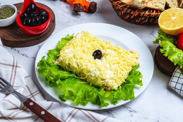 Insalata di mimosa vista laterale su lattuga con olive nere limone e verdure sul tavolo