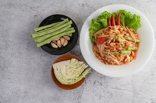 Insalata di papaia tailandese in un piatto bianco con fagioli yardlong, aglio e cavolo bianco