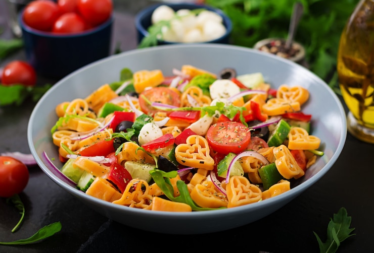 Foto gratuito insalata di pasta a forma di cuore con pomodori, cetrioli, olive, mozzarella e cipolla rossa alla greca.