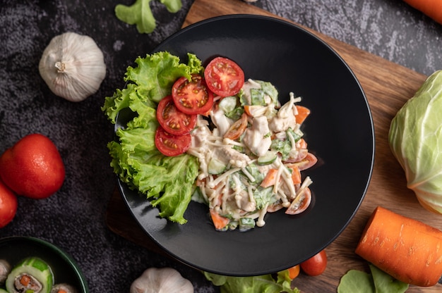 Insalata di pollo con pomodoro, funghi ago, carote, lattuga e cetriolo su un piatto nero