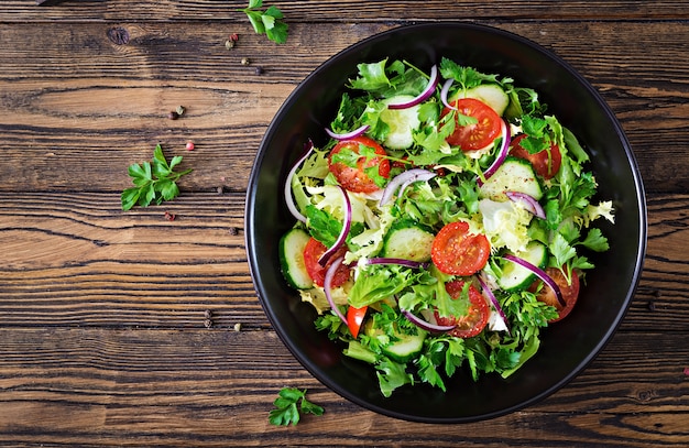 Insalata di pomodori, cetrioli, cipolle rosse e foglie di lattuga. Menù vitaminico estivo salutare. Alimenti vegetali vegani. Tavolo da pranzo vegetariano. Vista dall'alto. Disteso