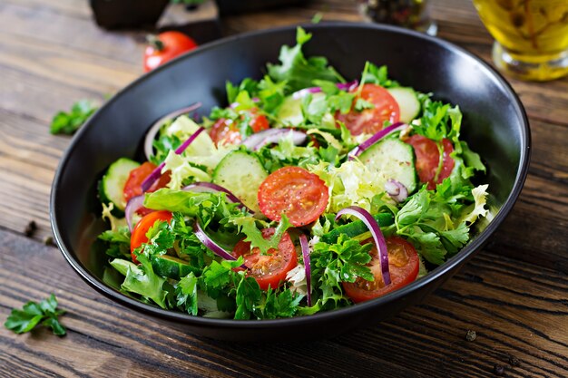 Insalata di pomodori, cetrioli, cipolle rosse e foglie di lattuga. Menù vitaminico estivo salutare. Alimenti vegetali vegani. Tavolo da pranzo vegetariano.