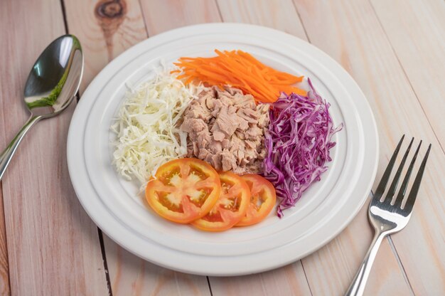 Insalata di tonno con carote, pomodori, cavolo su un piatto bianco su un pavimento di legno.