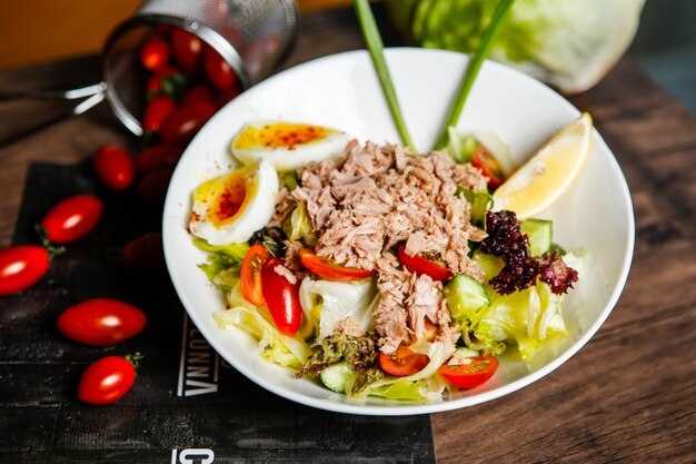 Insalata di tonno vista frontale con pomodori e uova sode in un piatto con il limone