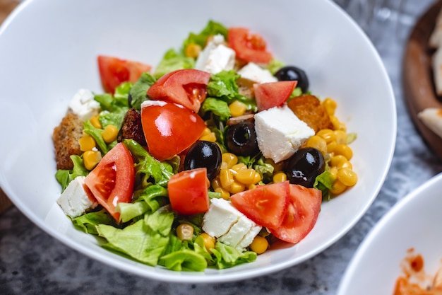 Insalata di verdure di vista laterale con la fetta biscottata della lattuga e del pane di olive nere del pomodoro del formaggio bianco