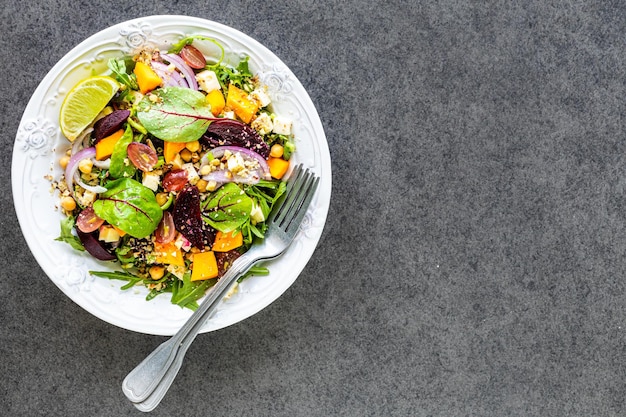 Insalata di verdure fresche con barbabietola rossa rucola cipolla rossa acetosa ceci zucca e uva in un piatto bianco su sfondo nero Vista dall'alto