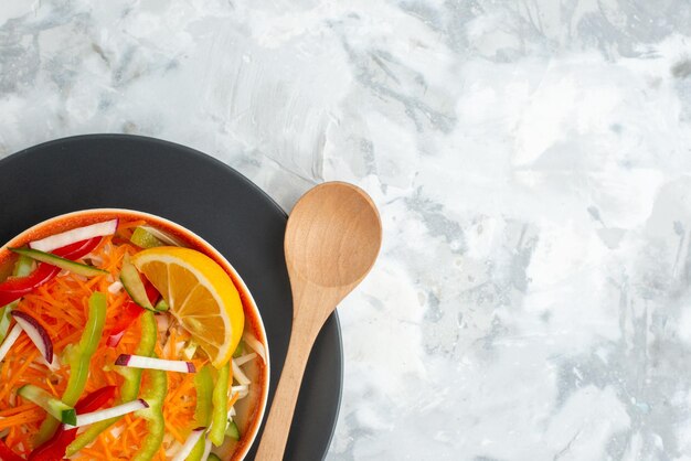 Insalata di verdure fresche vista dall'alto all'interno del piatto con cucchiaio di legno su superficie bianca pasto cibo cena orizzontale dieta salutare