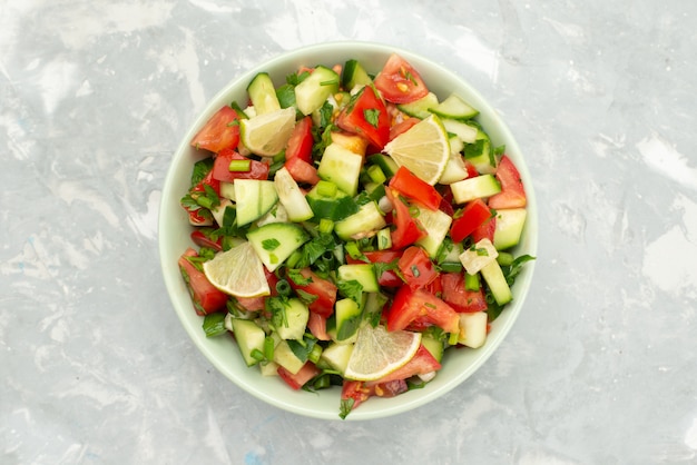 Insalata di verdure fresche vista dall'alto con verdure affettate e fette di limone all'interno del piatto rotondo sul blu