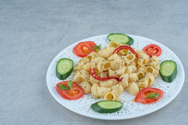 Insalata di verdure sul piatto bianco con deliziosi maccheroni su sfondo di marmo