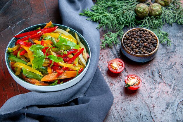 Insalata di verdure vista dal basso in una ciotola Pepe nero in una piccola ciotola Scialle blu oltremare del ramo di abete sul tavolo rosso scuro