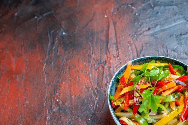 Insalata di verdure vista metà inferiore in una ciotola sul tavolo rosso scuro con posto libero free