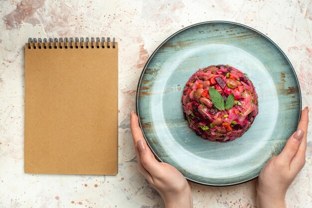 Insalata di vinaigrette vista dall'alto su piatto ovale in taccuino a mano femminile su tavolo grigio chiaro