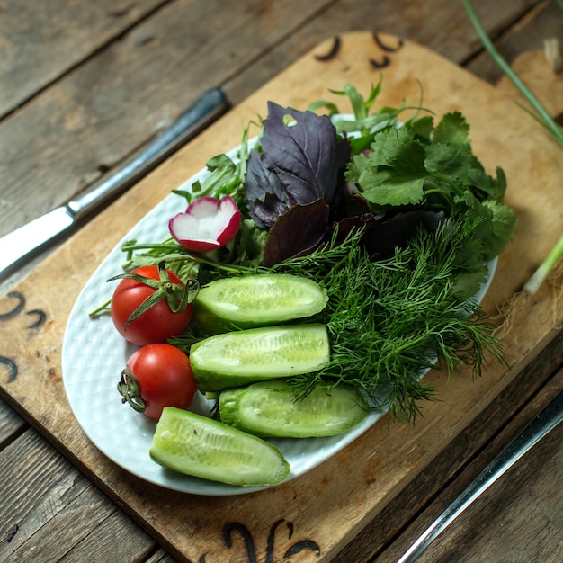 insalata fresca superiore con cetrioli pomodori ed erbe sul piatto su legno