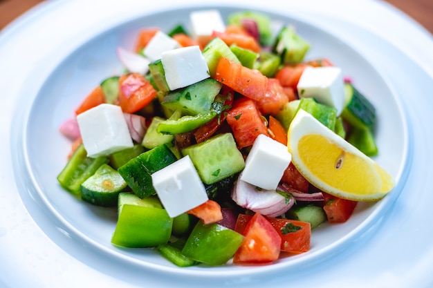 Insalata greca di vista laterale con il pomodoro fresco del cetriolo del formaggio bianco inverza la cipolla rossa e la fetta di limone su un piatto