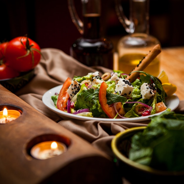 Insalata greca di vista laterale con le candele e pomodoro e verdi in piatto bianco rotondo