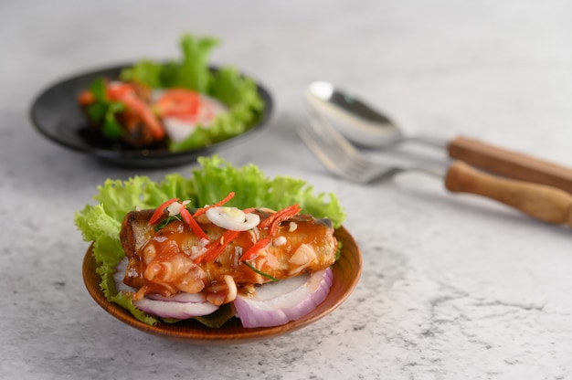 Insalata piccante appetitosa di sardine in scatola con salsa piccante in ciotola di legno