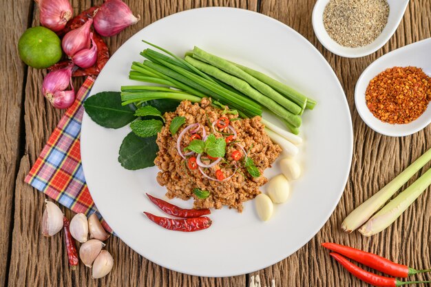 Insalata piccante di maiale macinato su un piatto bianco con cipolla rossa, citronella, aglio, fagioli, foglie di lime kaffir e cipollotto