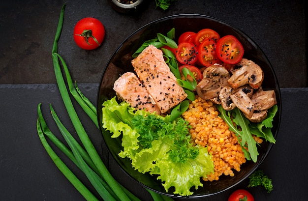 Insalata sana con salmone, pomodori, funghi, lattuga e lenticchie su oscurità