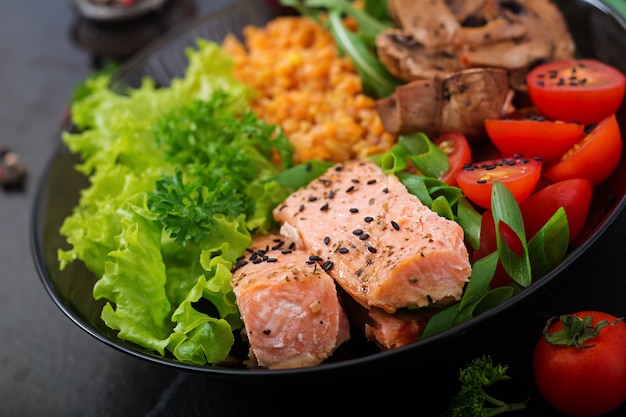 Insalata sana con salmone, pomodori, funghi, lattuga e lenticchie su oscurità