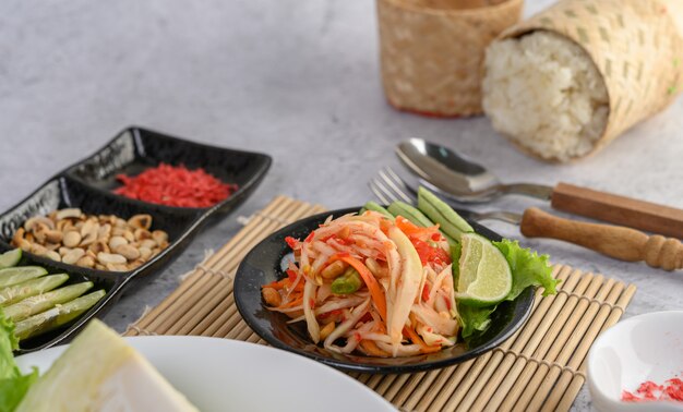 Insalata tailandese della papaia in un piatto bianco con riso appiccicoso e gamberetti essiccati